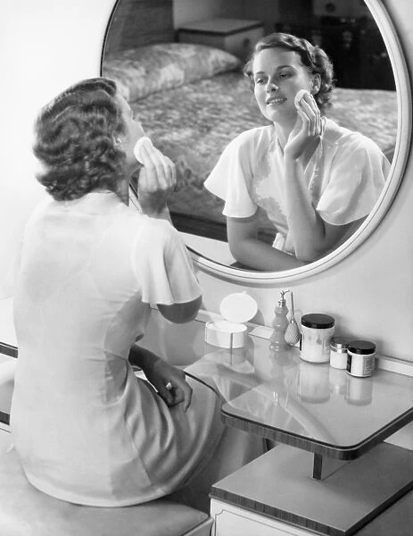 Woman applying powder with powder puff in front of mirror, (B&W)