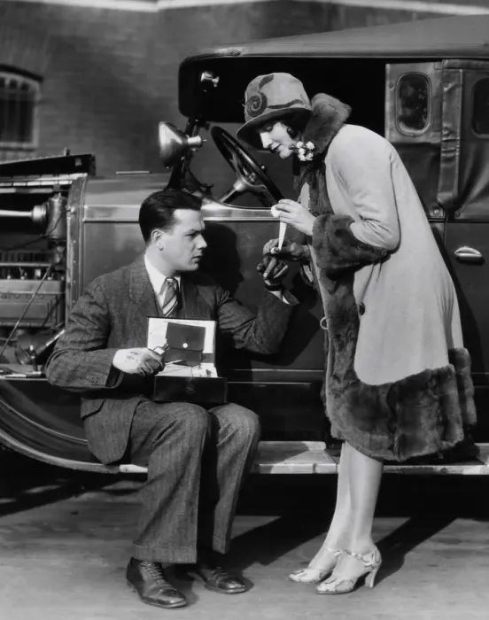 Framed Print : Woman bandaging finger of man with greasy hands, sitting on running board of car with hood open Framed Print : Woman bandaging finger of man with greasy hands, sitting on running board of car with hood open
