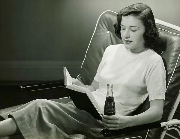 Woman with bottle of beverage, reading book, (B&W)