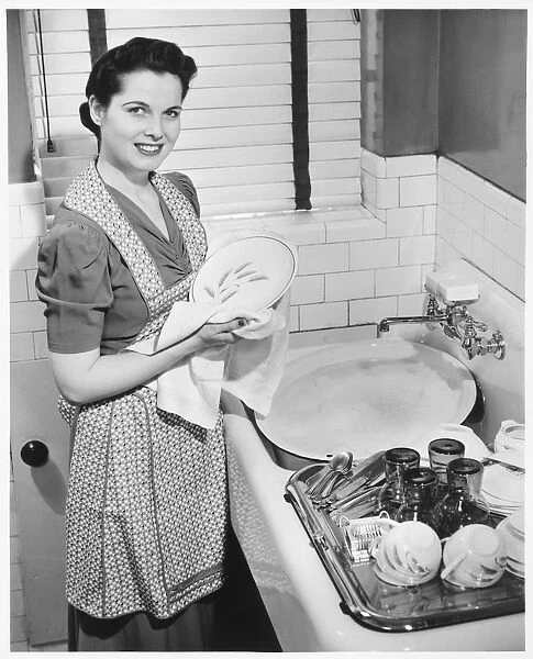 Woman drying dishes at kitchen sink, (B&W), elevated view