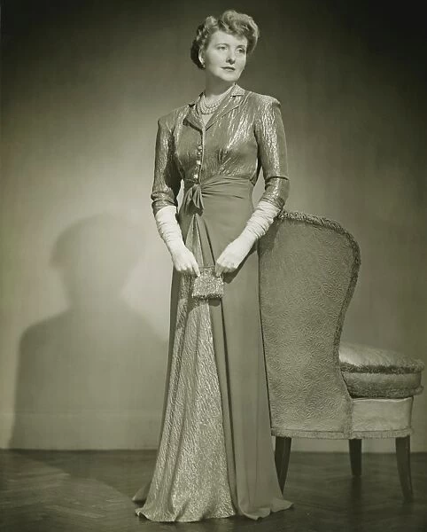 Woman in evening dress standing indoors, (B&W)