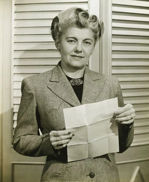 Woman in fashionable suit holding sheet of paper, indoors, (B&W)