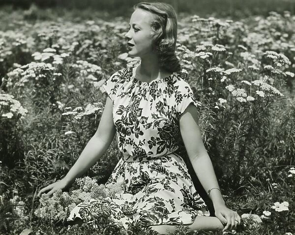Woman in flowery dress sitting in meadow among flowers, (B&W), portrait