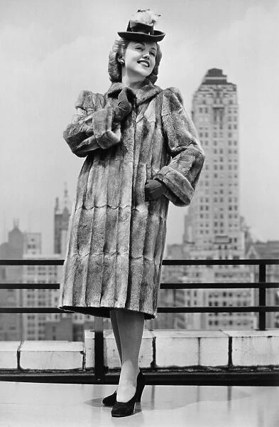 Woman in fur coat and fancy hat standing on outside terrace (B&W)