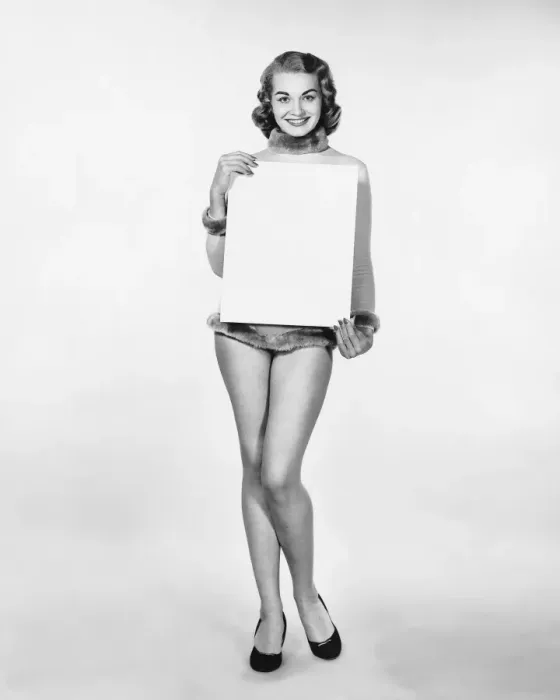 Framed Print : Woman in fur-trimmed leotard holding blank poster Framed Print : Woman in fur-trimmed leotard holding blank poster