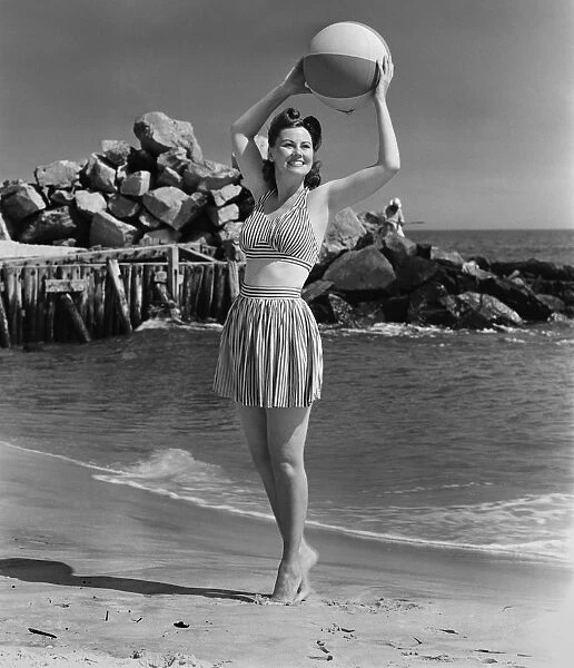 Woman holding ball on beach, (B&W)