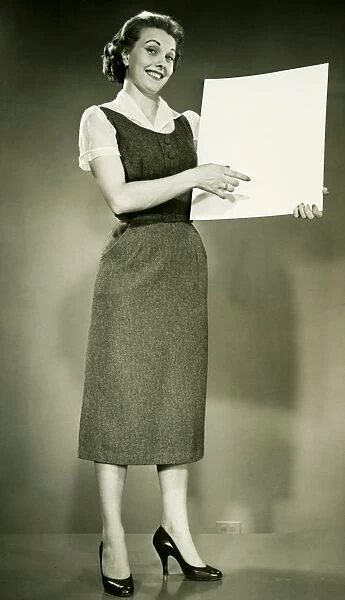 Woman holding blank sheet of paper, posing in studio, (B&W), portrait