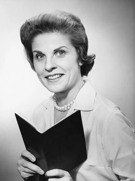 Woman holding notebook, smiling, (B&W), portrait