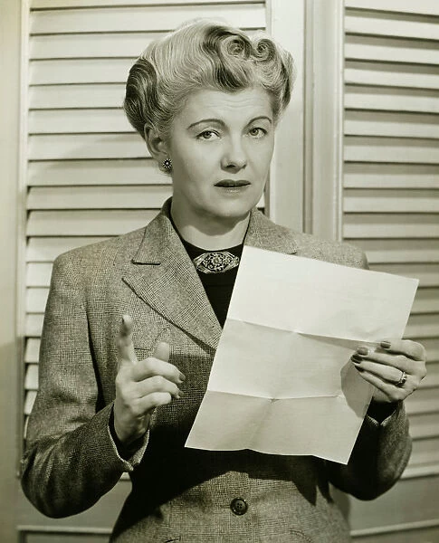 Woman holding sheet of paper, pointing, (B&W), portrait
