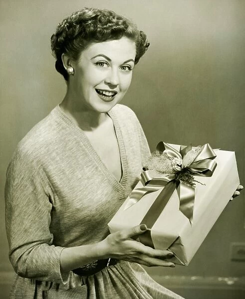 Woman holding wrapped gift in studio, (B&W), portrait