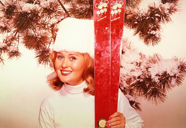 WOMAN HOLDS UP A PAIR OF SKIS, 1960S
