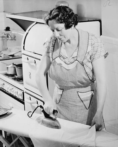 Woman ironing in kitchen, (B&W)