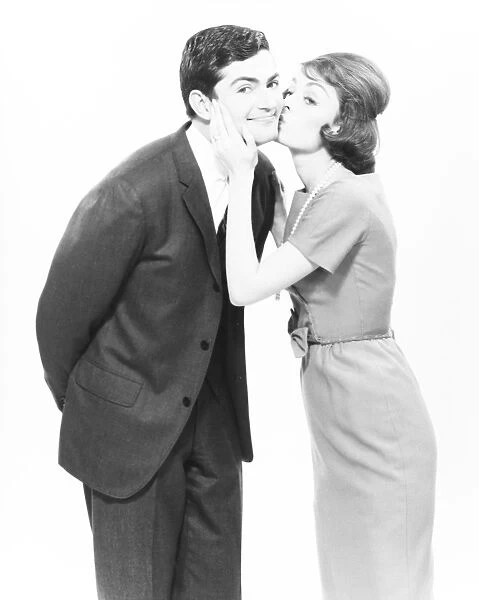 Woman kissing man on cheek in studio, (B&W)