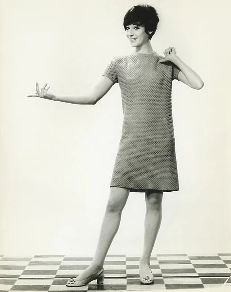 Woman in knitted dress gesturing in studio, (B&W), portrait