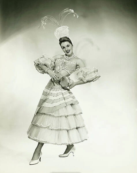 Woman in Latino dance costume posing in studio, holding drum, (B&W)