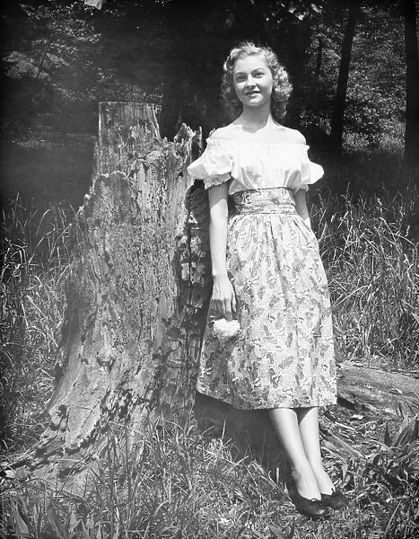 Woman leaning against tree trunk in forest, (B&W), (Portrait)