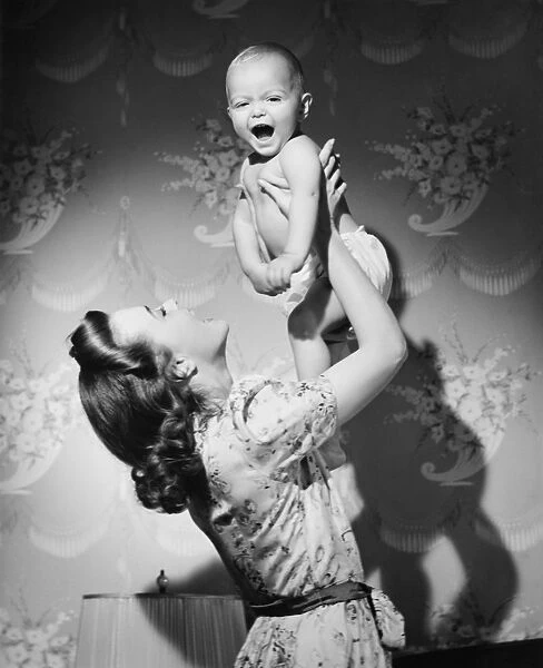 Woman lifting up baby (6-9 months) at home, (B&W)