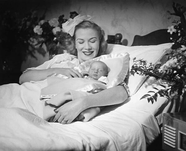 Woman lying on bed, holding new born baby (B&W)