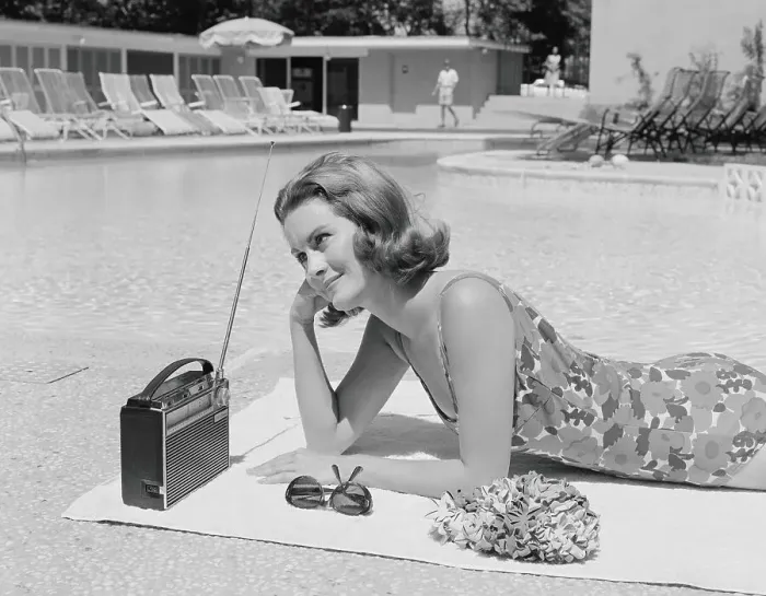 Framed Print : Woman lying on towel poolside listening to radio with antenna up