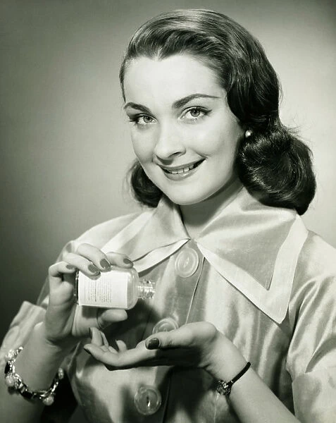 Woman pouring pills from bottle into hand in studio, (B&W), portrait