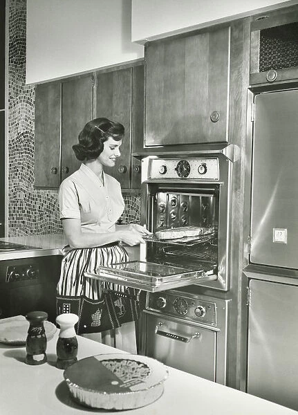 Woman putting meal into oven in kitchen, (B&W)