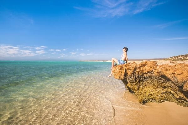 Woman with sarong and straw hat sunbathing at Osprey Bay, Cape Range National Park, Exmouth, Western Australia