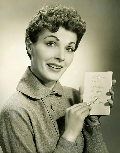 Woman showing shopping list in studio, (B&W), portrait