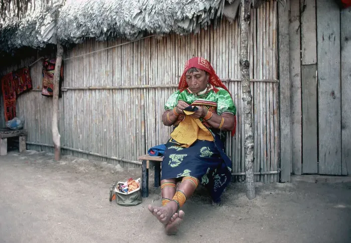 Framed Print : Woman Sits in Front of Hut Sewing Framed Print : Woman Sits in Front of Hut Sewing