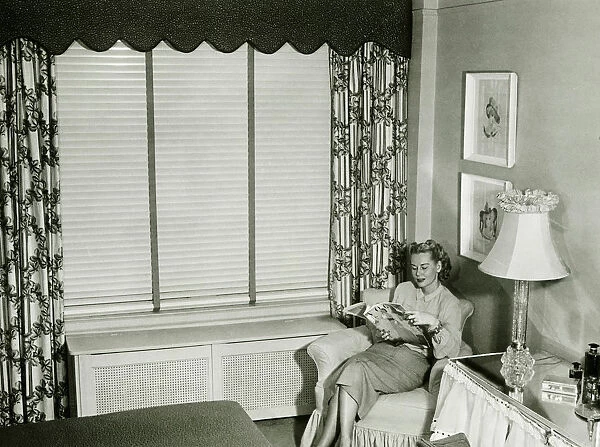Woman sitting on armchair in bedroom, reading fashion magazine (B&W)