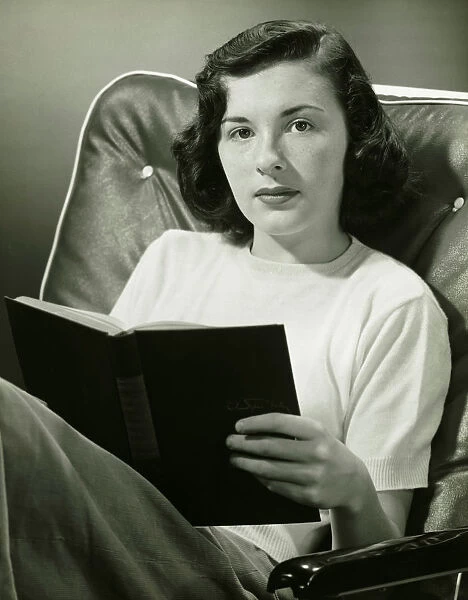 Woman sitting on armchair, holding book, (B&W), (Portrait)