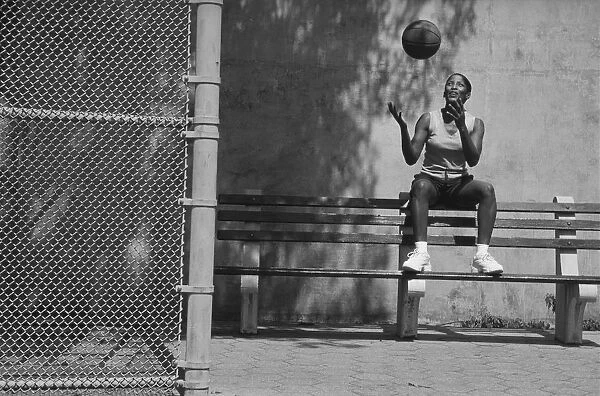 Woman sitting on bench tossing basketball in air (B&W)