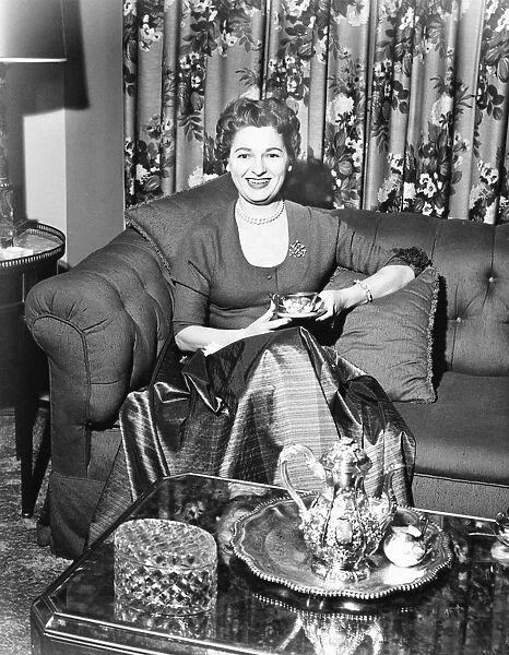 Woman sitting in rich living room, holding cup of coffee, (B&W)