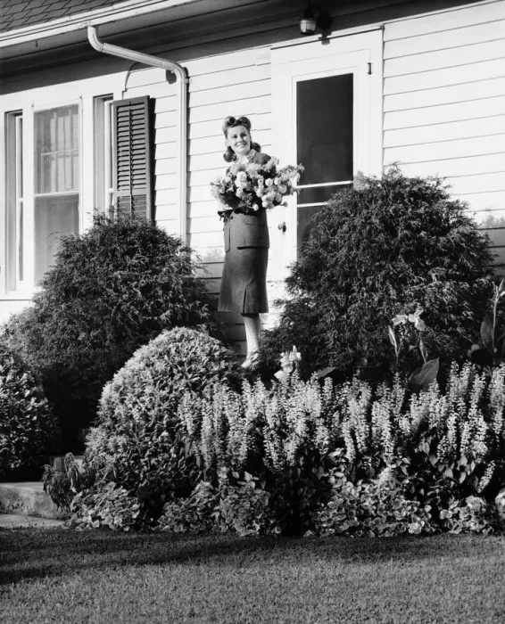 Framed Print : Woman standing on front porch of house holding bunch of flowers, (B&W) Framed Print : Woman standing on front porch of house holding bunch of flowers, (B&W)