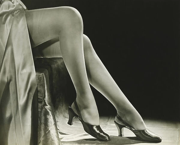 Woman in stockings sitting on chair, close-up of legs, (B&W), low section