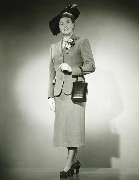 Woman in suit and fashionable hat standing in studio, (B&W)