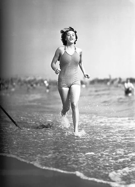 Woman in swimsuit running on shoreline, (B&W)
