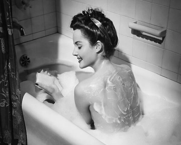 Woman taking bubble bath, holding soap bar, (B&W)