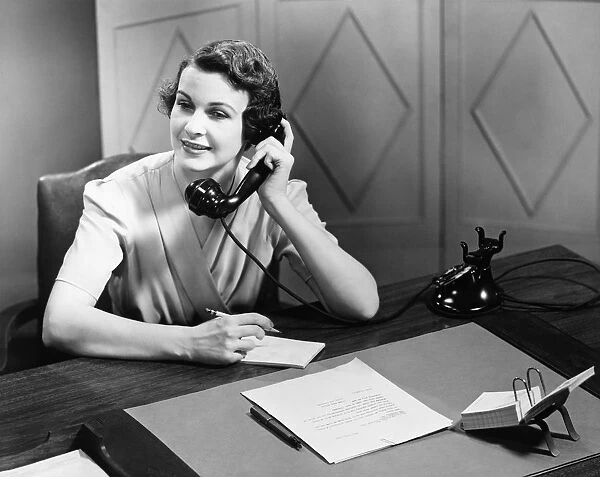 Woman talking on phone at desk (B&W)