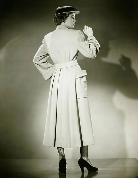 Woman in trench coat and hat posing in studio (Rear view), (B&W)