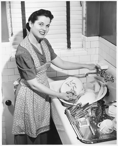 Woman washing dishes in kitchen sink, (B&W), elevated view