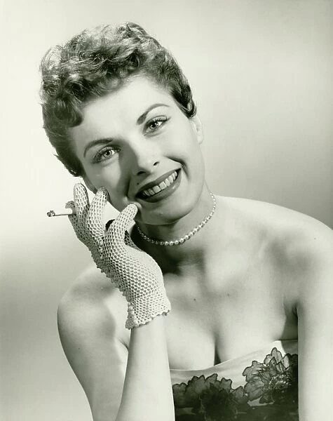 Woman wearing lace glove holding cigarette in studio, (B&W), portrait