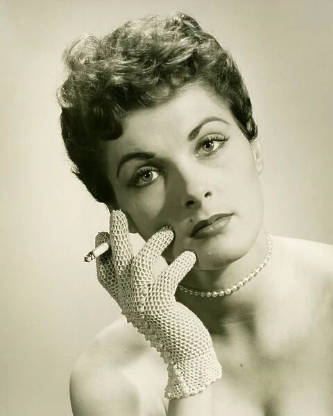 Woman wearing lace glove holding cigarette in studio, (B&W), portrait