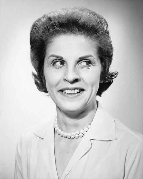 Woman wearing pearls smiling, looking away, posing in studio, (B&W), portrait