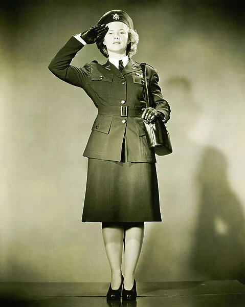 Woman wearing World War II uniform saluting in studio, (B&W), portrait