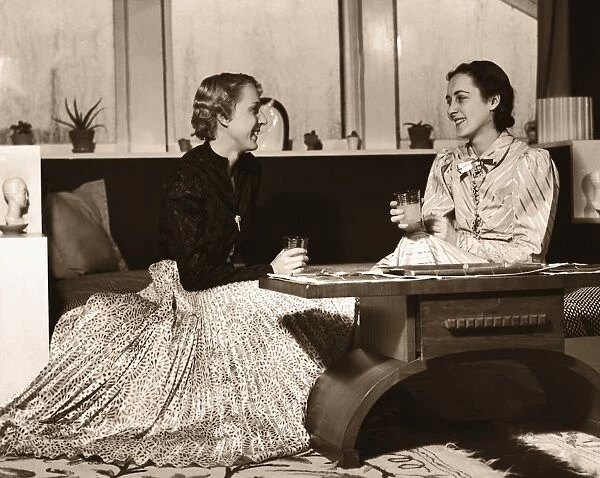 Two Women Sitting on Sofa with Drinks, Chatting
