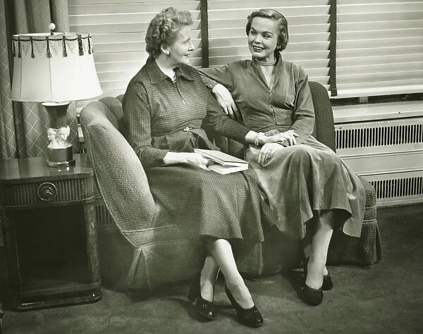 Two women sitting on sofa, talking, indoors, (B&W)