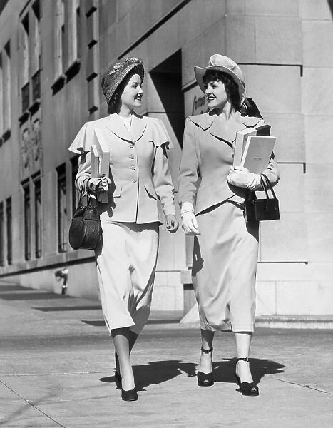Two women walking along sidewalk in city