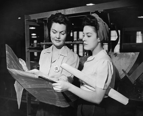 Two women in workshop looking at blueprints, (B&W)