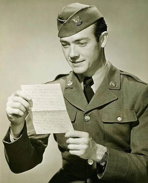 World War II Army solider reading letter in studio, (B&W), portrait