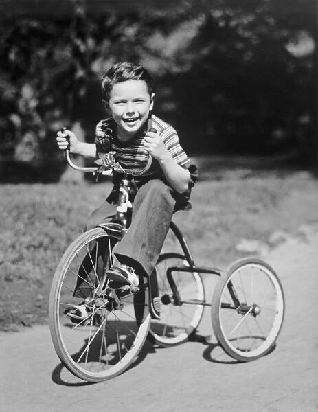 Young boy (6-7) riding tricycle in park, (B&W), portrait